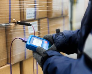 Hand of worker using thermometer to temperature measurement in the goods boxes with ready meals after import in the cold room or warehouse for keep temperature room