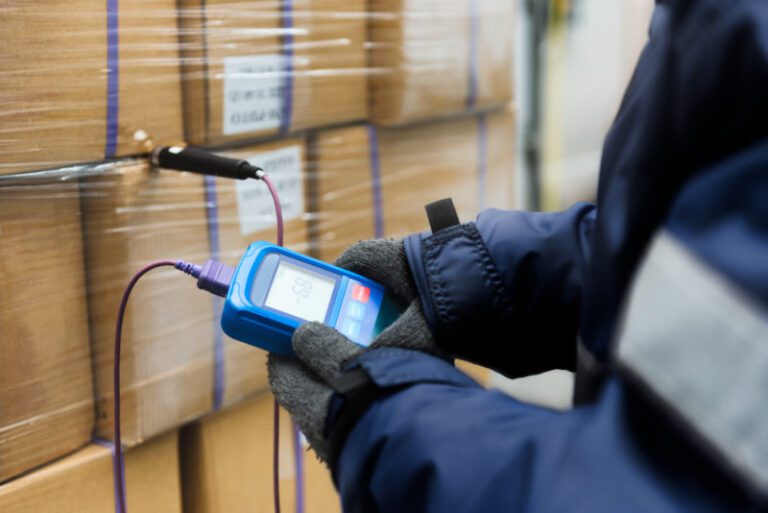 Hand of worker using thermometer to temperature measurement in the goods boxes with ready meals after import in the cold room or warehouse for keep temperature room